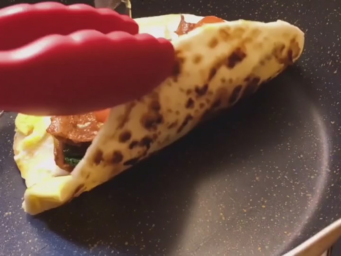 A freshly prepared scallion flatbread wrap being rolled tightly on a flat surface.