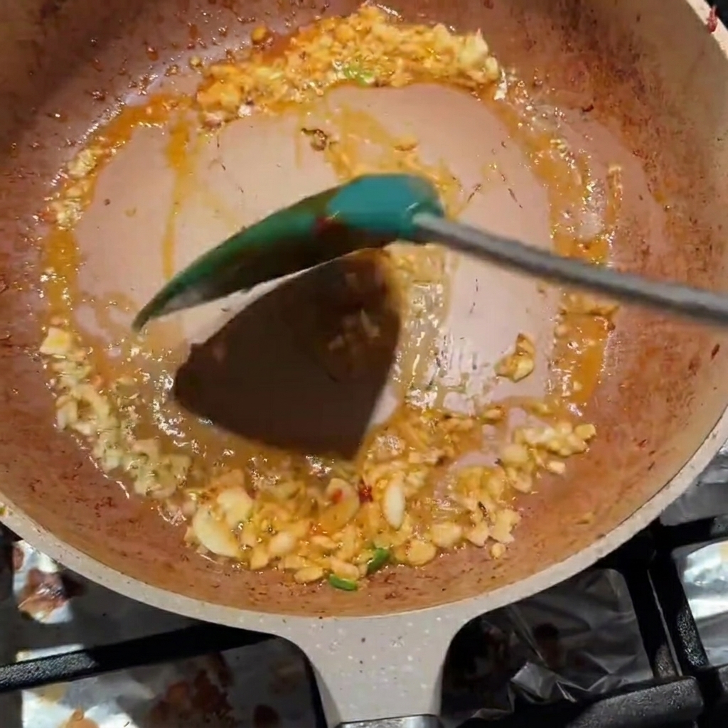 Minced garlic and Pixian bean paste being stirred together in a pan.