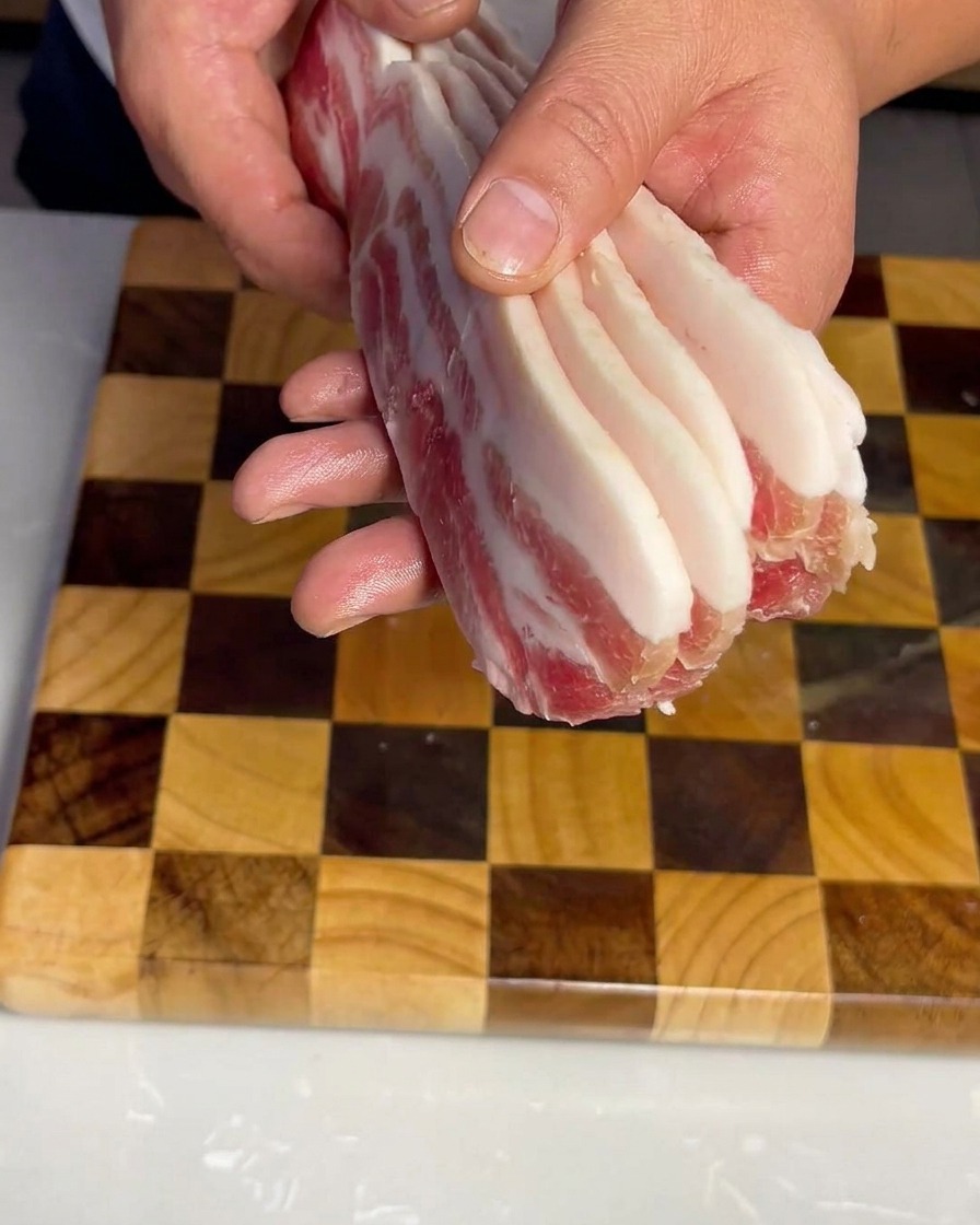 Uniform strips of raw pork belly neatly arranged on a wooden cutting board.
