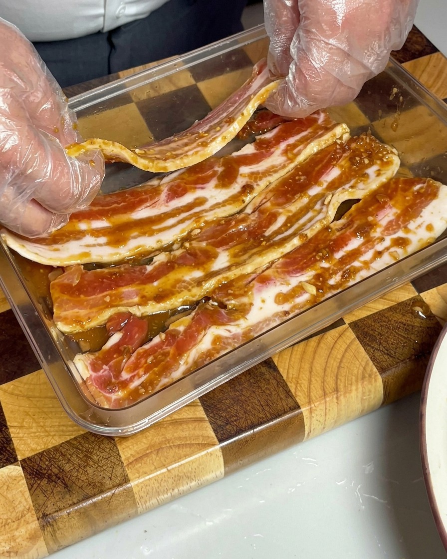 Marinated pork belly strips neatly laid out in a transparent container, fully submerged in the brown miso sauce.