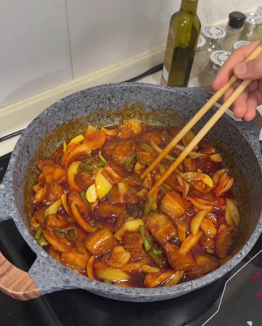 The finished spicy stir-fried pork belly dish with visible golden-brown meat, glistening sauce, and a light scattering of white sesame seeds on top.