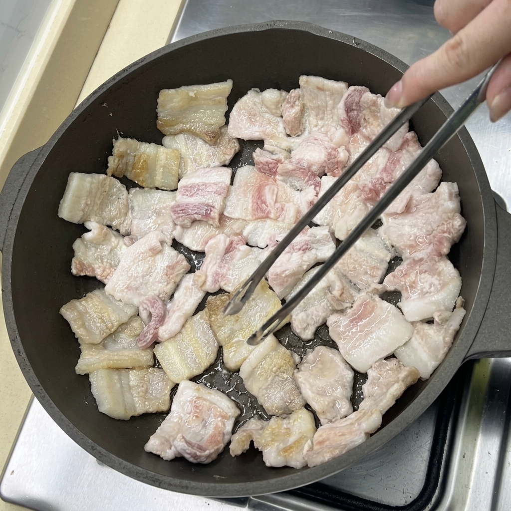 Pork belly slices frying in a pan, turning golden brown as the fat renders out.