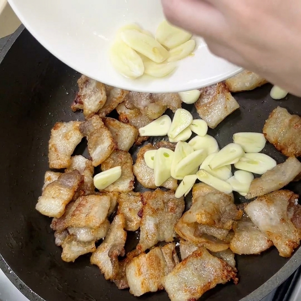 Fresh garlic slices added to the pan with the golden-brown pork belly.