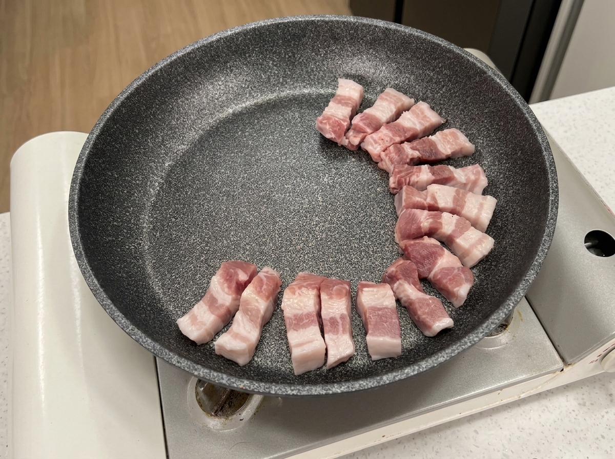 Raw pork belly slices arranged in a circular formation in a grey non-stick pan.