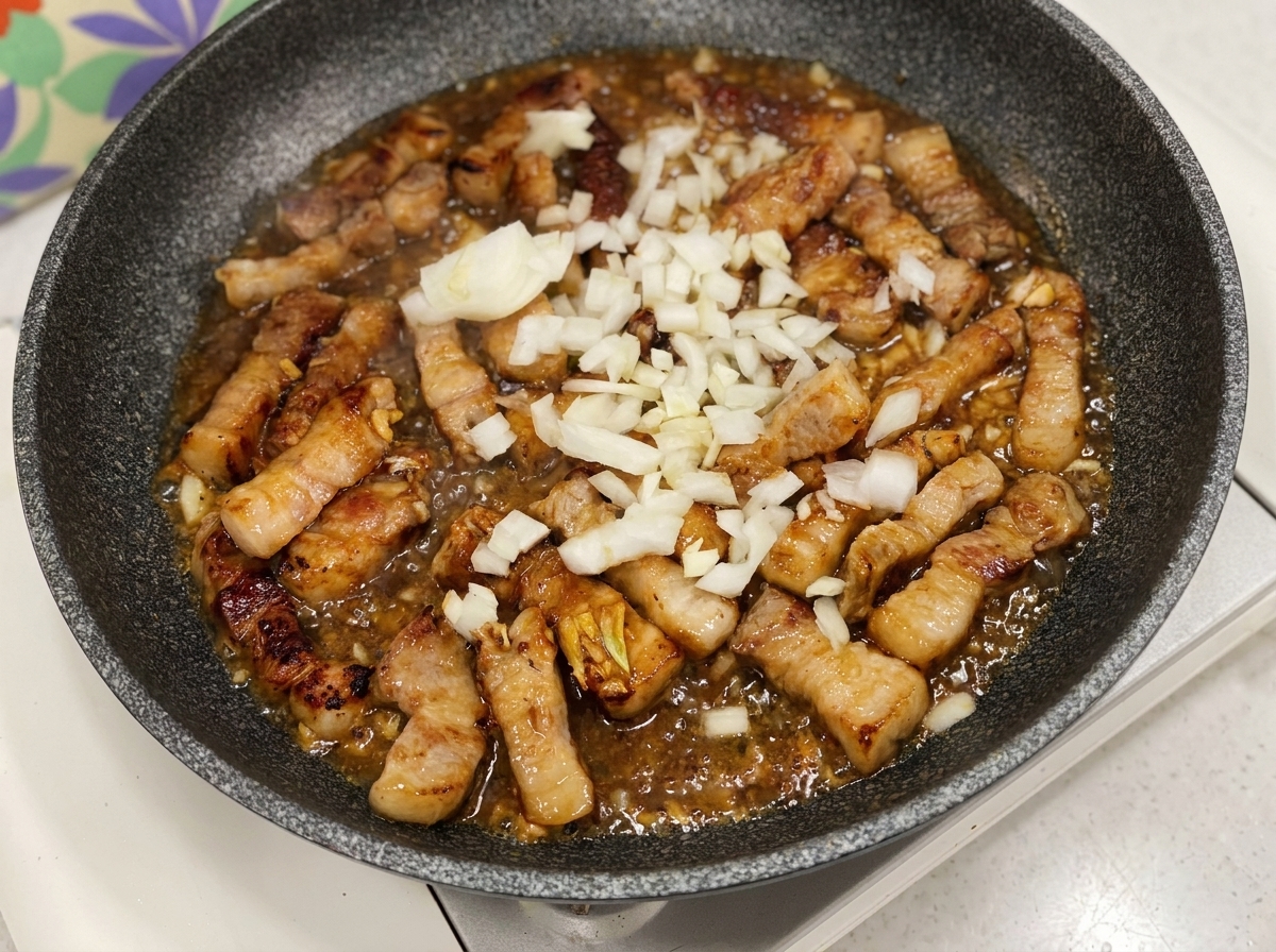 Chopped white onions added to a pan with pork and a bubbling dark sauce.