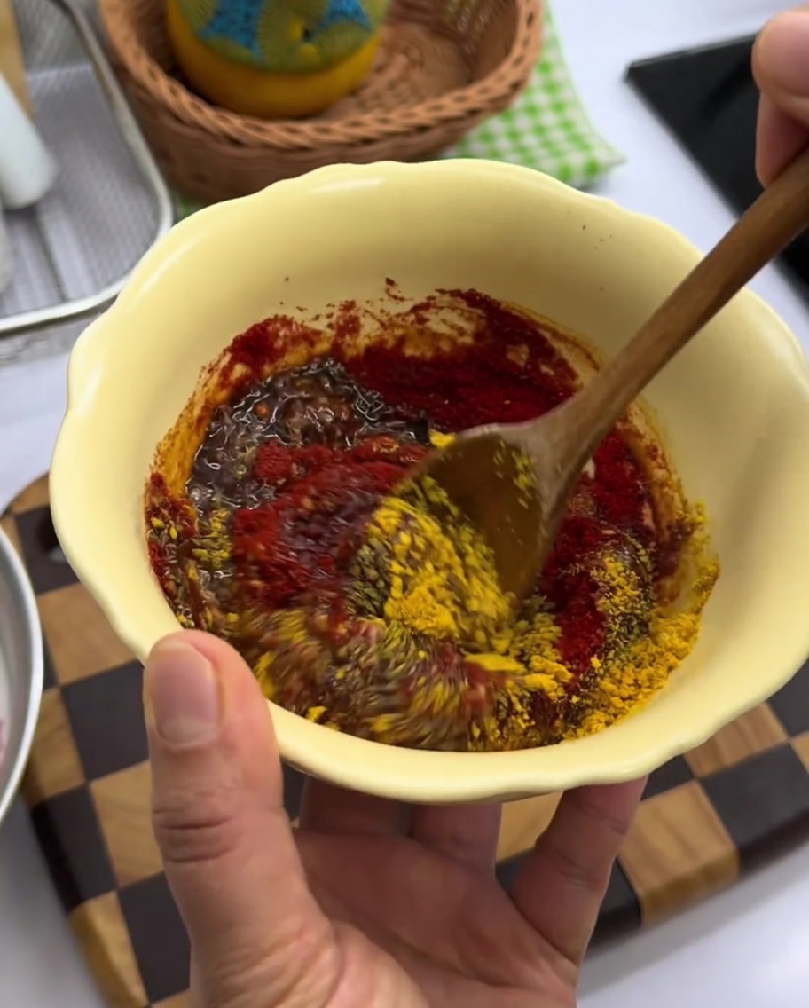 Thick red spice paste being stirred in a yellow mixing bowl.