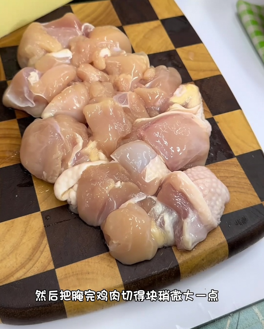 Uniform chunks of raw chicken thigh meat on a wooden cutting board.