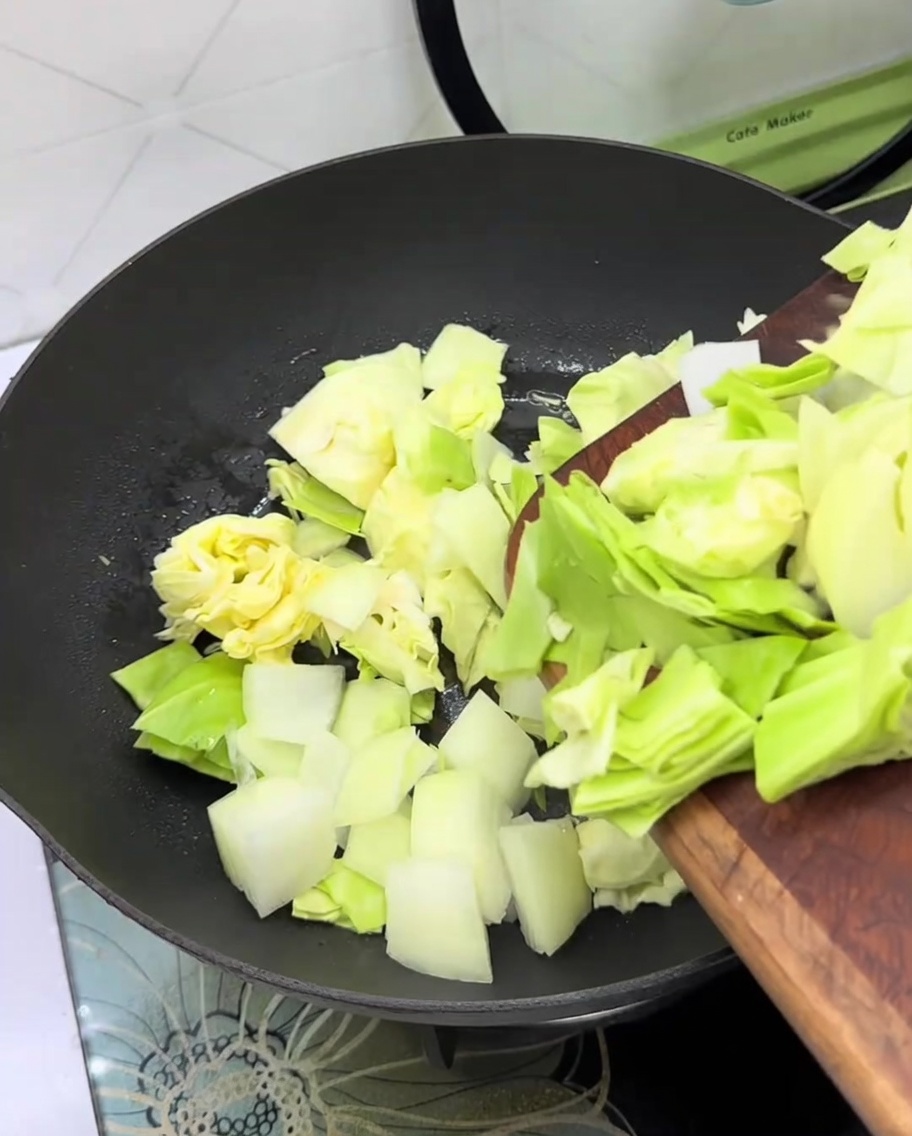 Fresh cabbage and sliced onion being added to an empty frying pan.