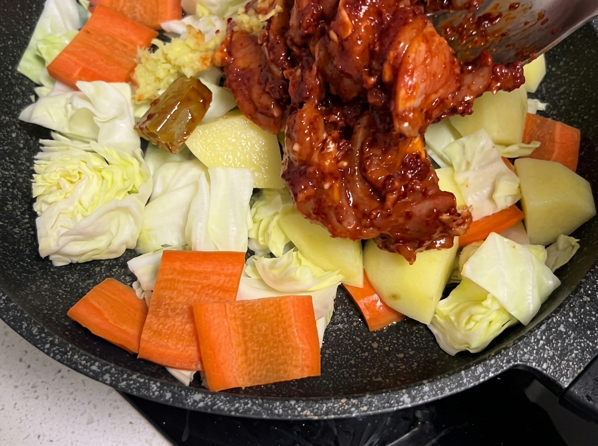 Marinated chicken pieces being carefully placed over the bed of vegetables in the skillet.