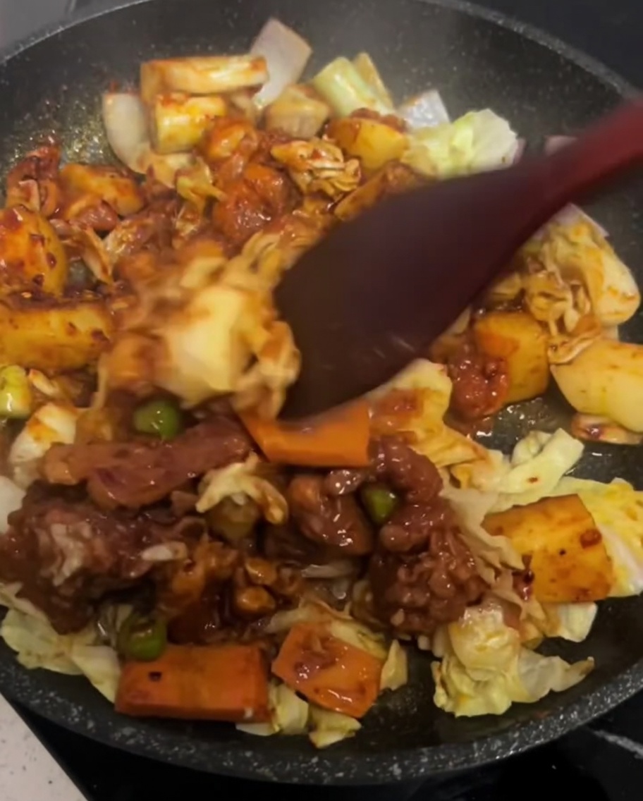 A spatula gently tossing the chicken and vegetables together in a hot pan.