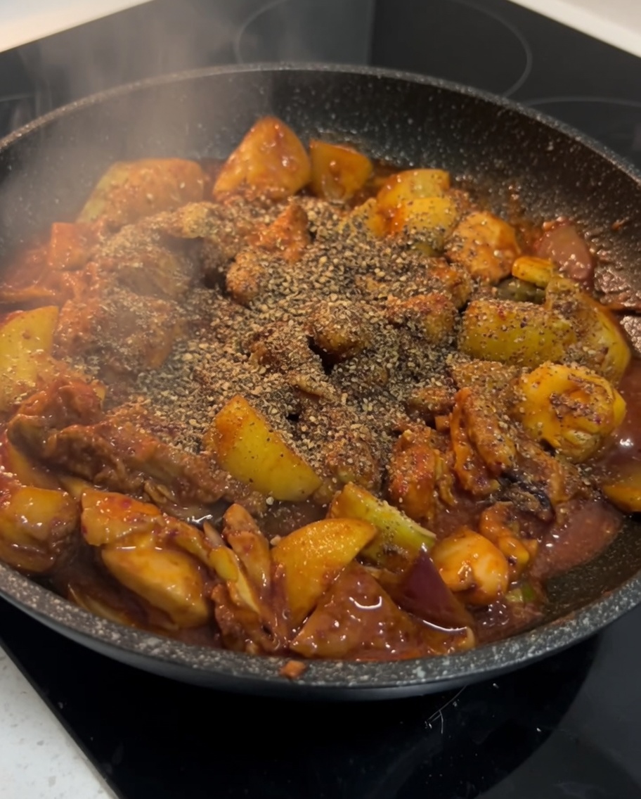 Finishing the Korean spicy chicken by seasoning it with perilla powder in the skillet.