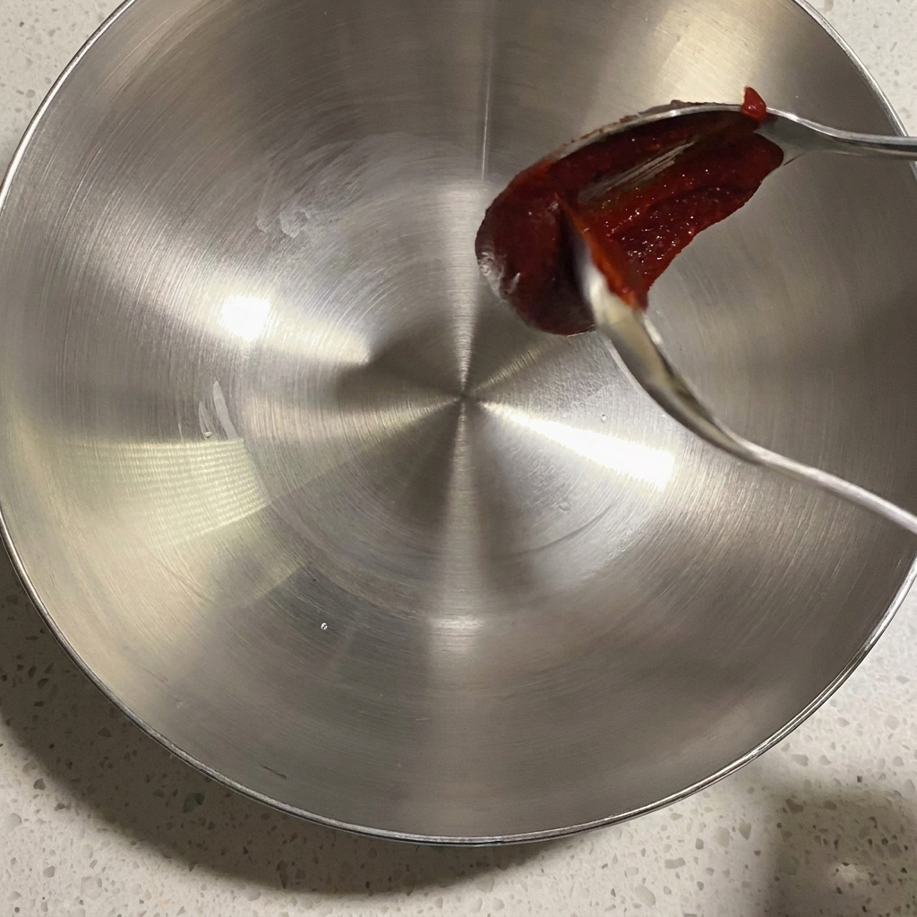 A close-up of a metal bowl containing various seasonings and sauces ready to be mixed.
