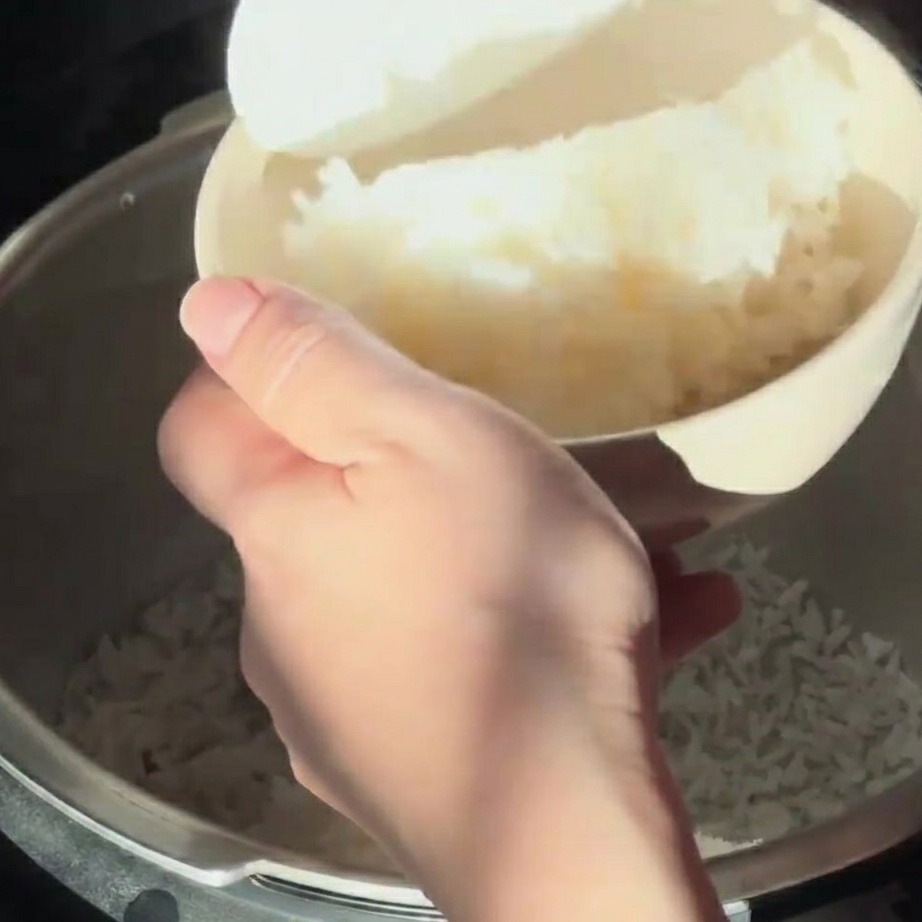 Steamed white rice being scooped into a light-colored bowl with a white rice paddle.