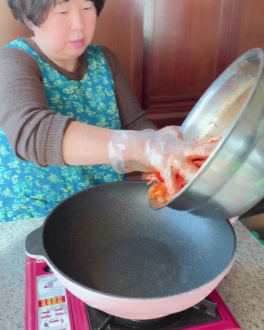 Marinated pork belly and squid mixture being poured from a stainless steel bowl into a hot pan.