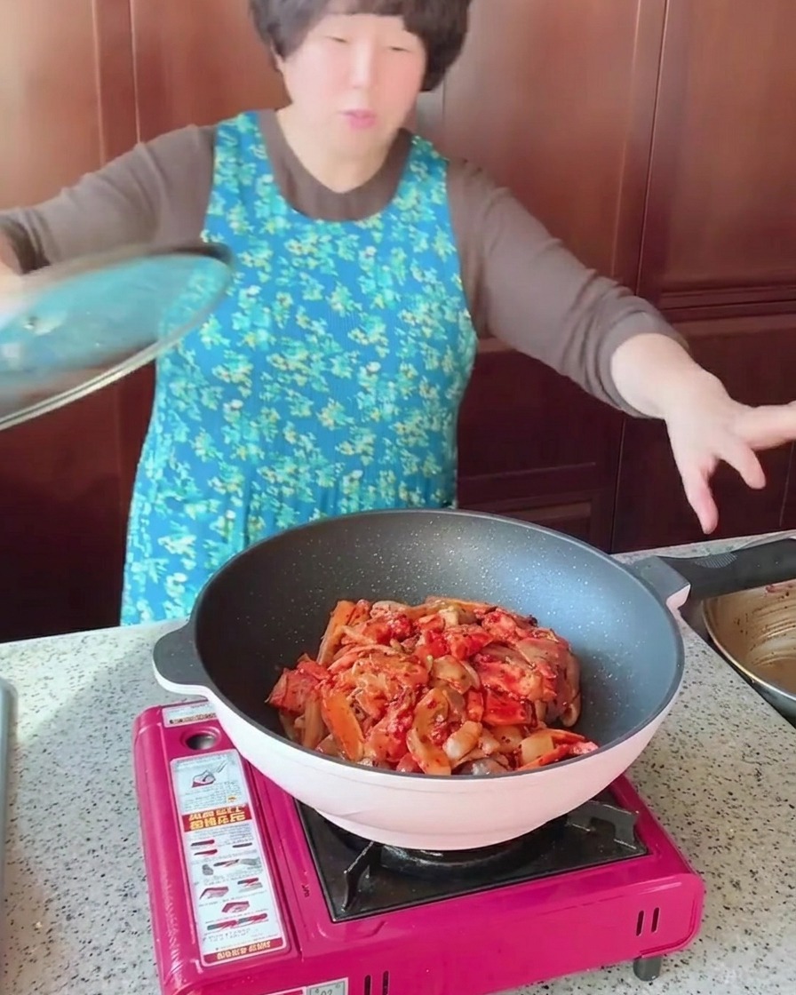 A pan filled with stir-fried pork belly, squid, and vegetables being covered with a clear glass lid.