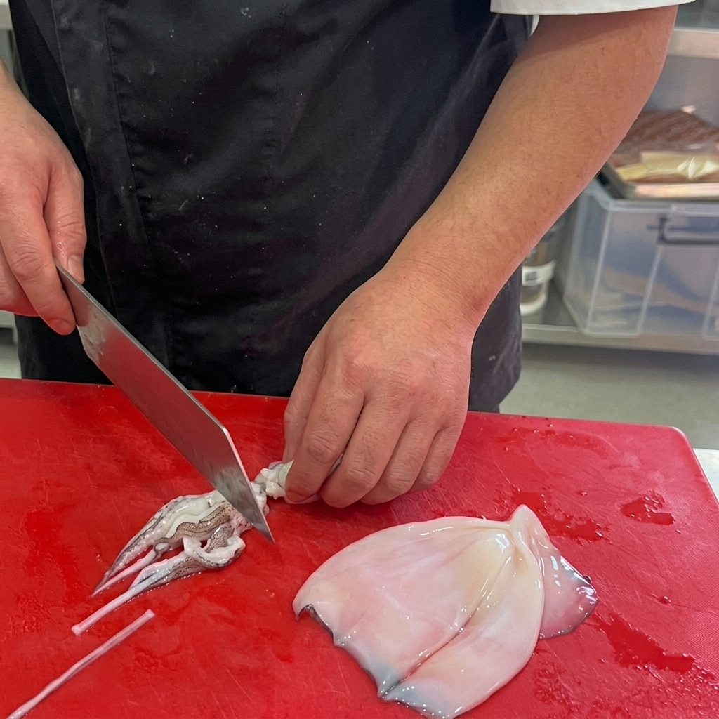 Cleaned squid being sliced into rings on a red cutting board.