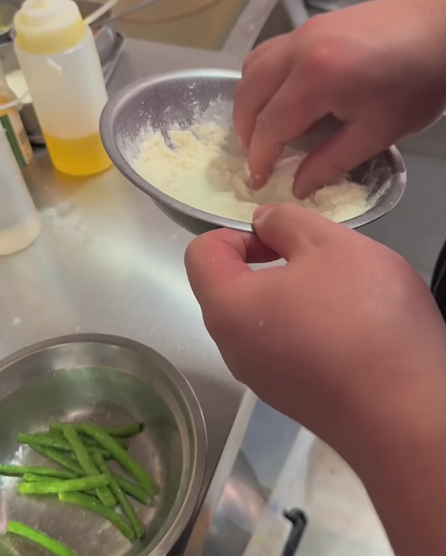 Green beans being tossed with flour and seasoning in a metal bowl.