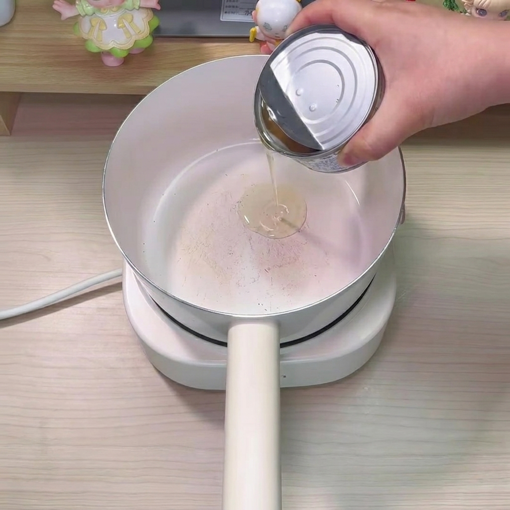 Golden tuna oil pouring from a metal can into the bottom of a white pot.