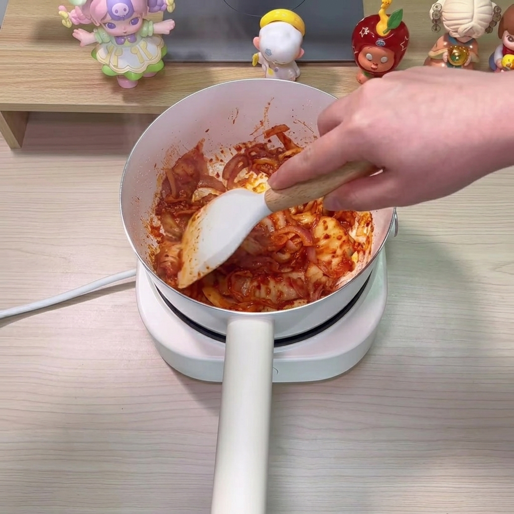 Clear water being poured into the pot, combining with the stir-fried kimchi and onions.