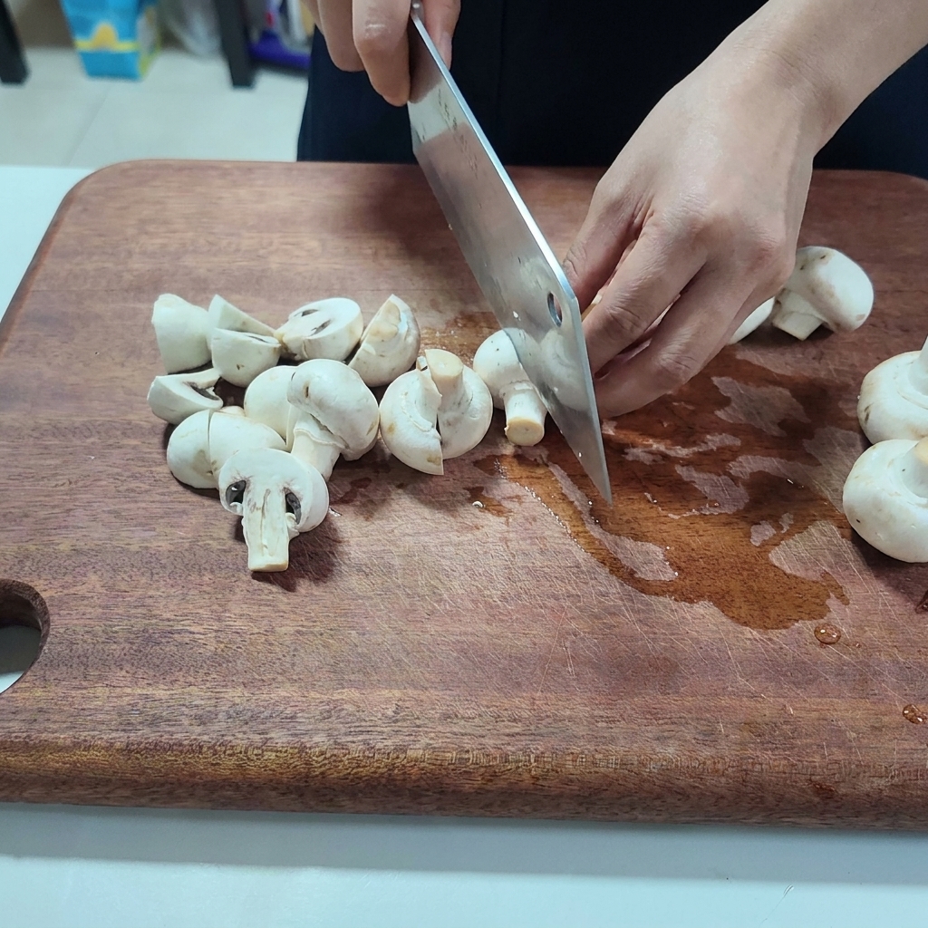 Fresh white mushrooms being sliced into halves on a wooden cutting board.