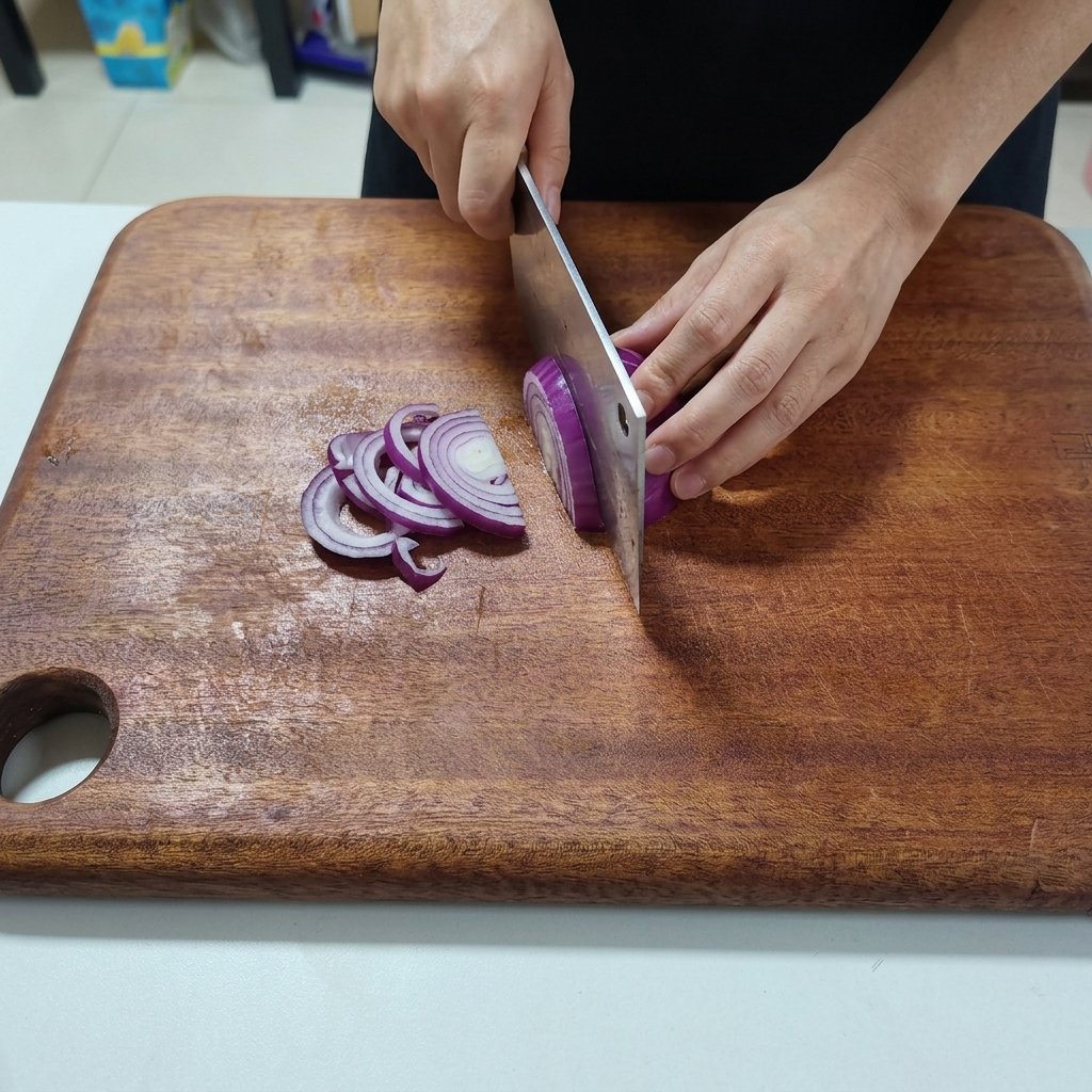 Red onion being sliced into thin strips on a wooden cutting board.