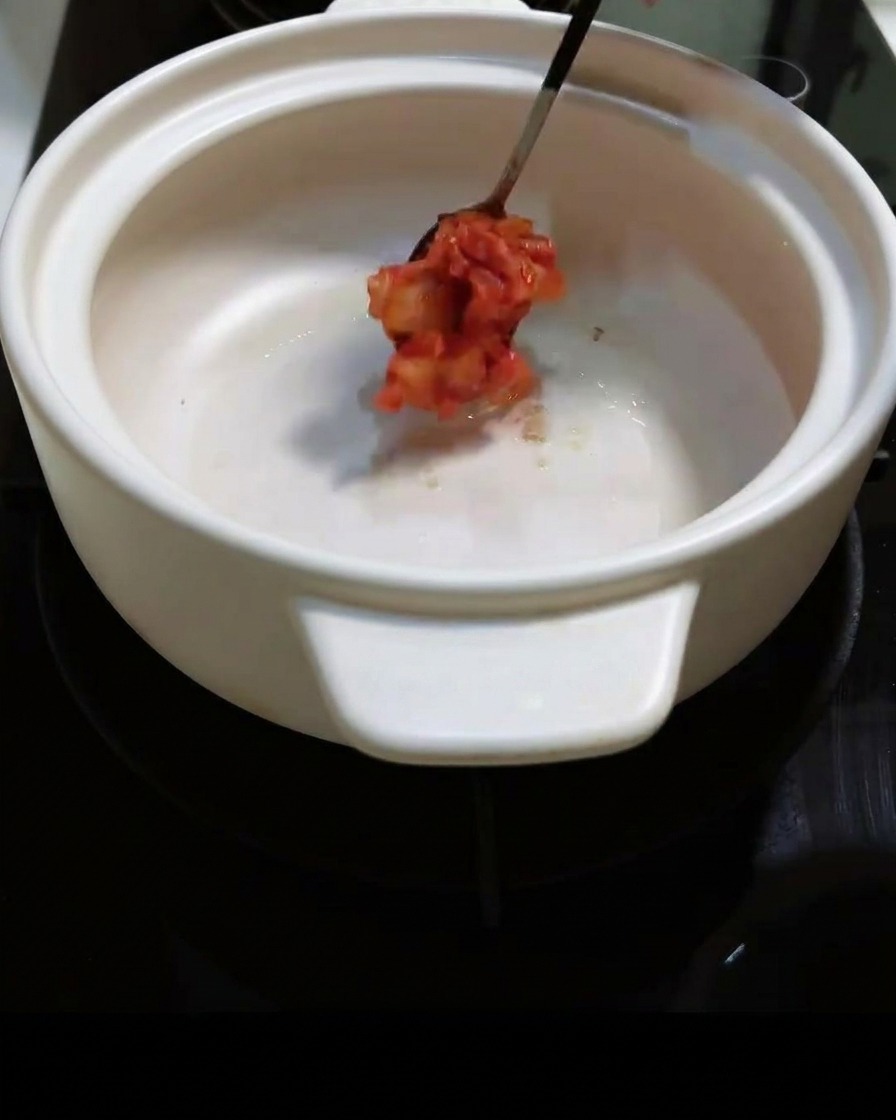 Chopped spicy kimchi being added to the pot and stirred.