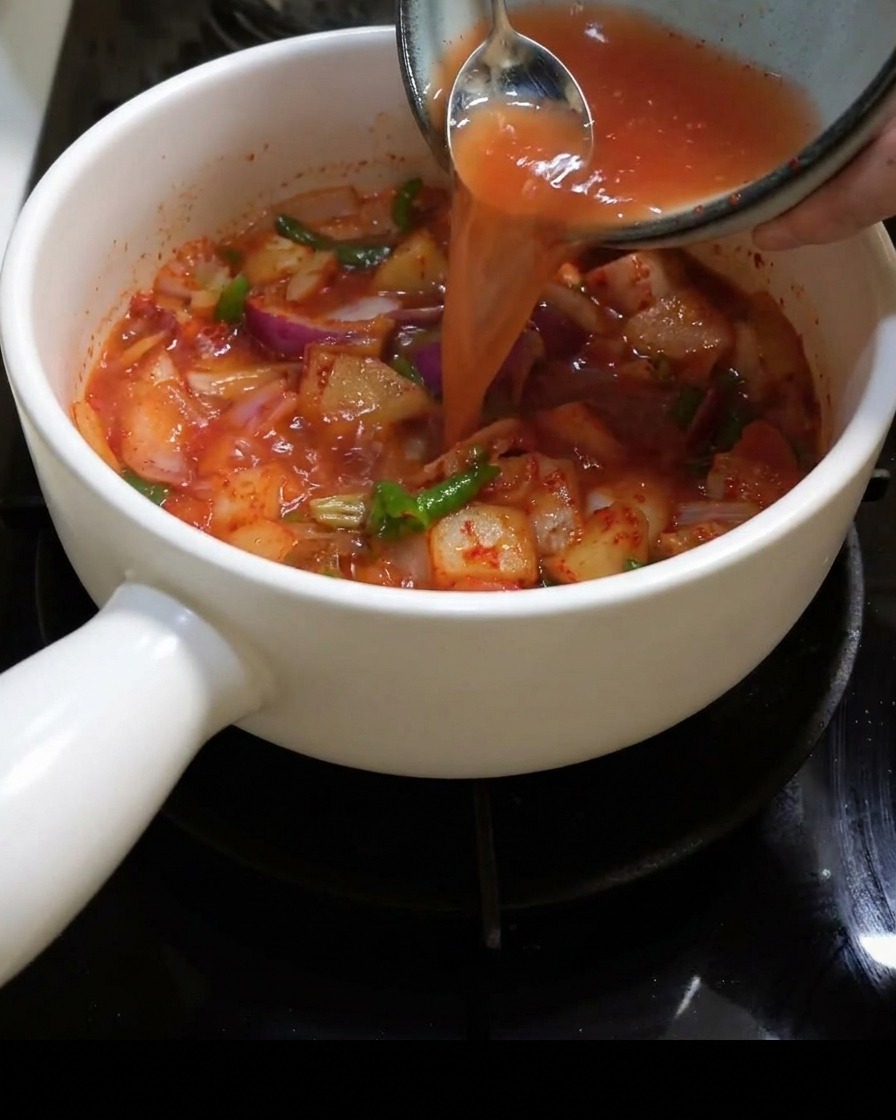Water being poured into the pot filled with kimchi and onions.