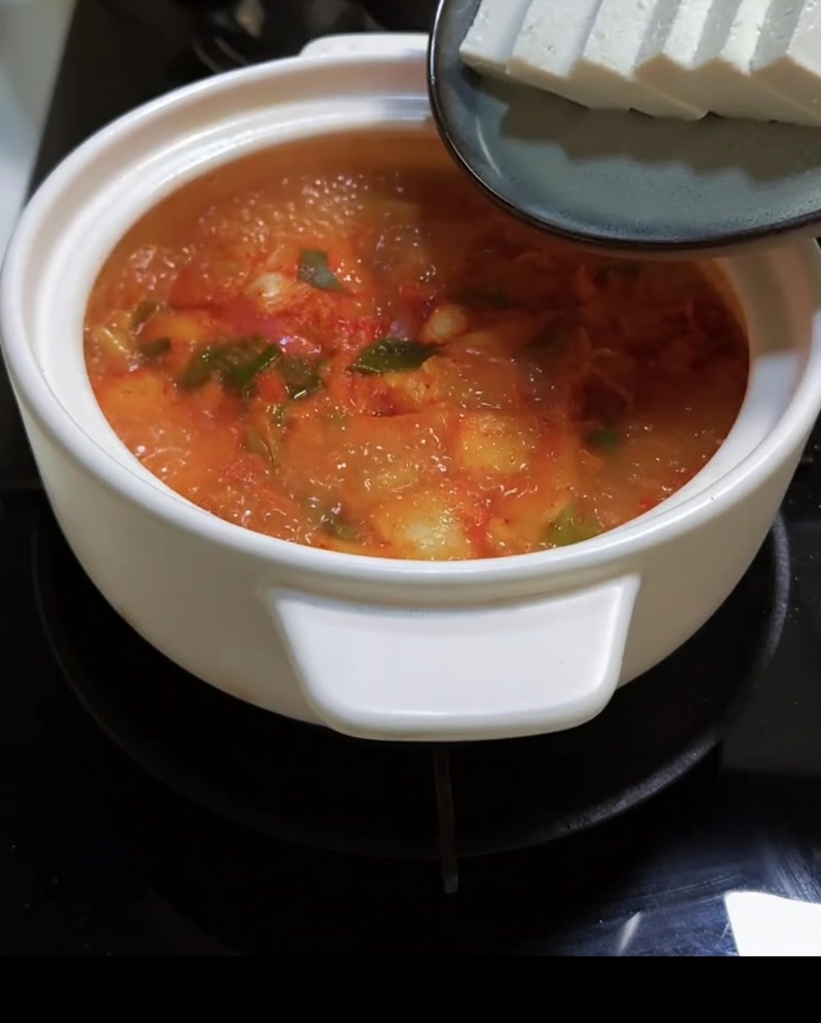 Sliced tofu being added to the bubbling red kimchi soup.