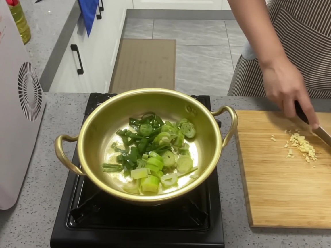 Green onions and garlic being sautéed in a golden pot with oil.