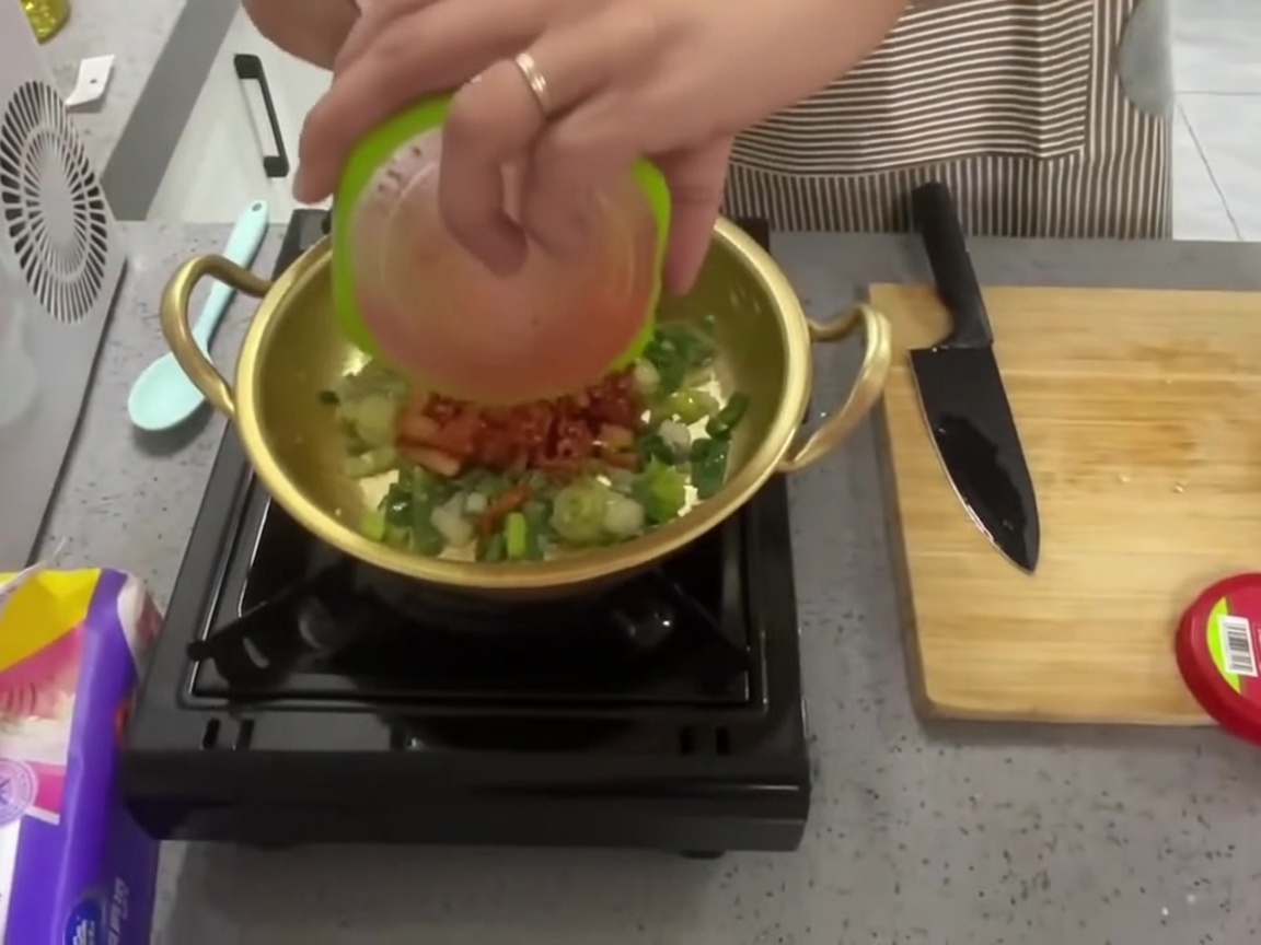 Chopped red kimchi being poured into the pot over the sautéed aromatics.