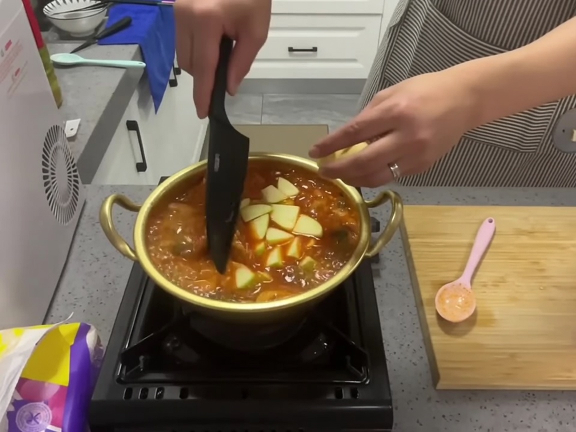 Slices of fresh green zucchini being added to a pot of boiling red kimchi stew.