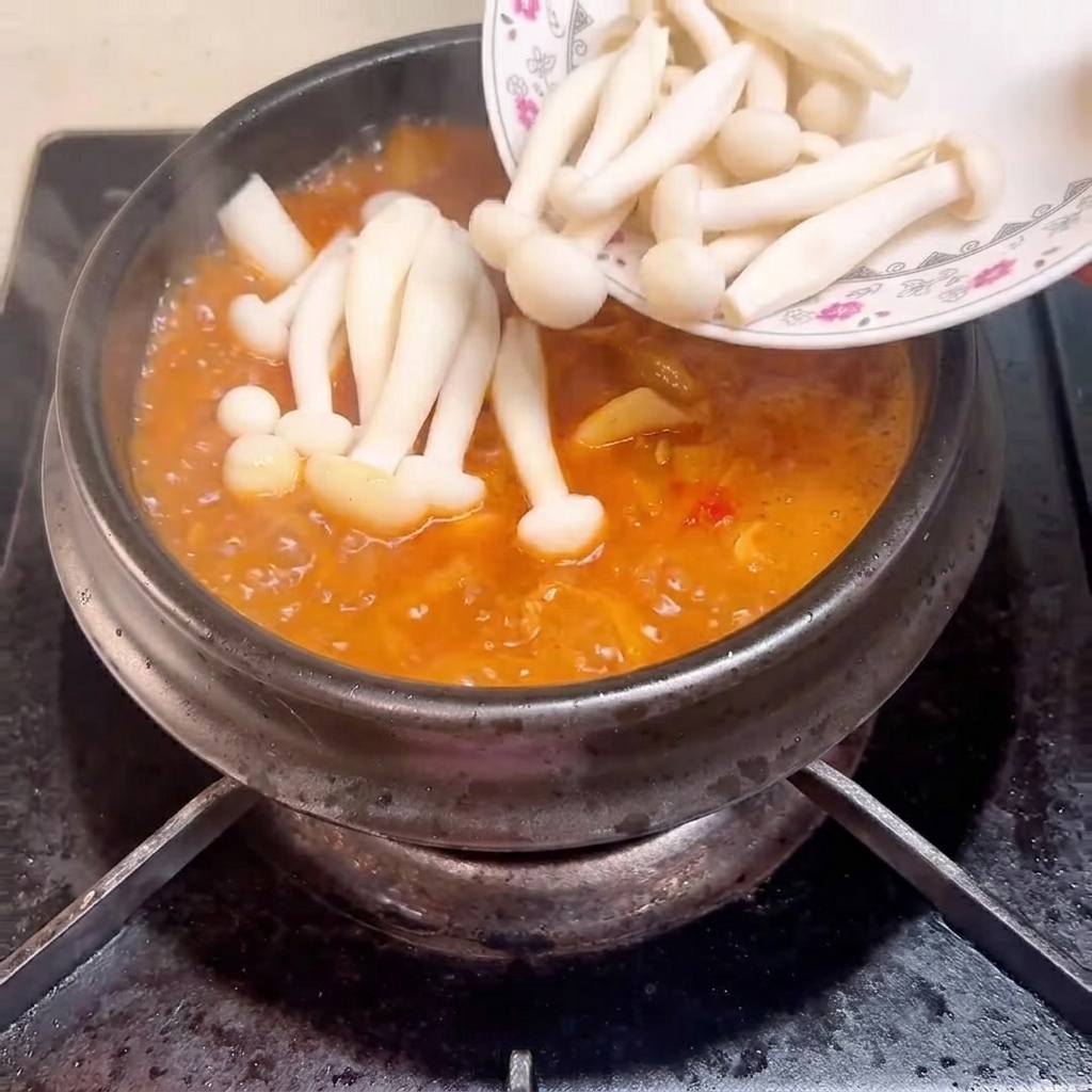 Seafood mushrooms being placed into the bubbling soup in the clay pot.