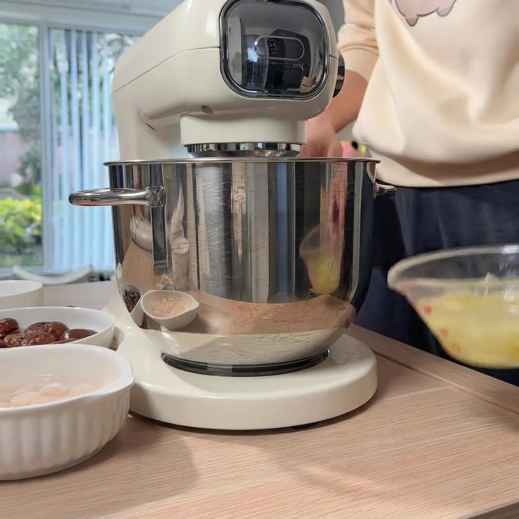 A hand pouring prepared ginger-scallion water from a glass bowl into the stand mixer bowl containing the ground chicken.