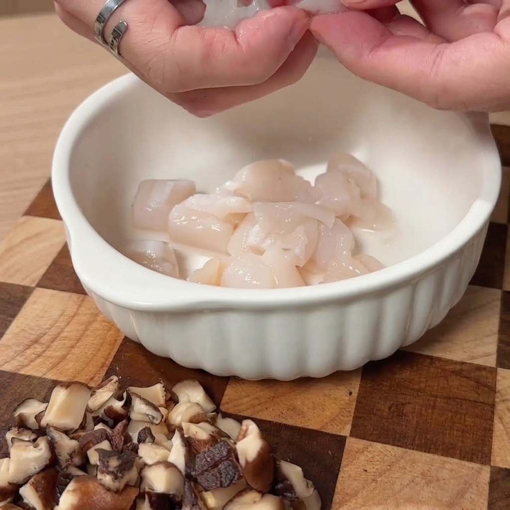 Dried scallops being carefully shredded by hand into thin strands over a small white bowl.
