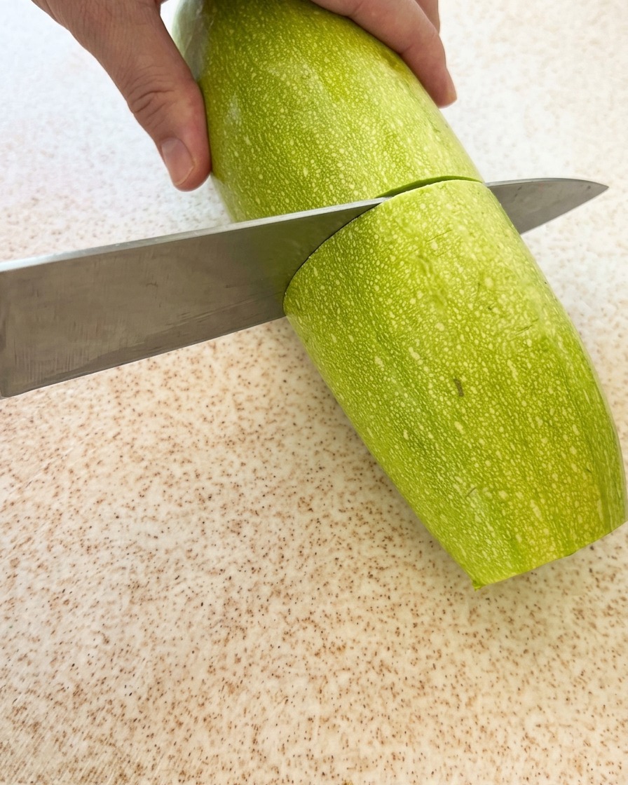 A fresh green zucchini being sliced into pieces on a cutting board.