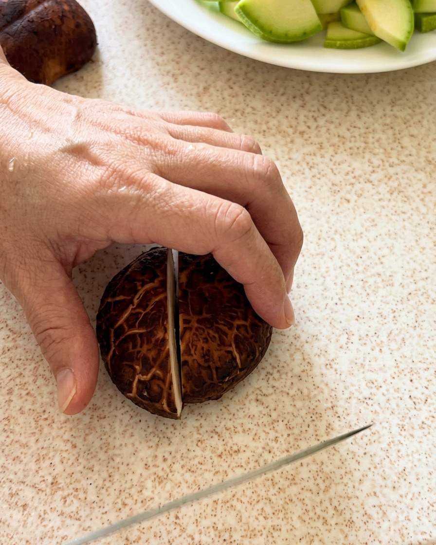 Shiitake mushrooms being carefully sliced on a cutting board.