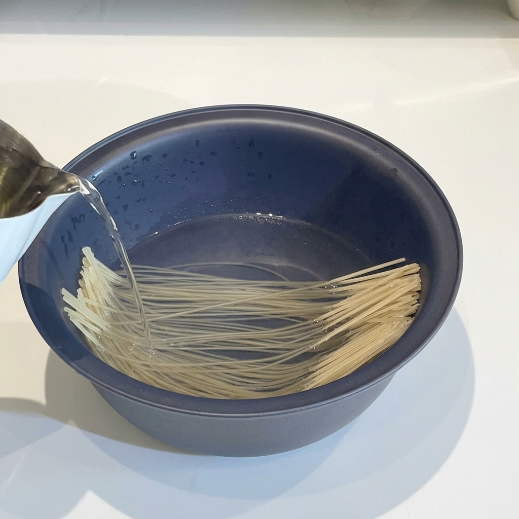 Glass noodles submerged in a bowl of hot water, appearing softened.