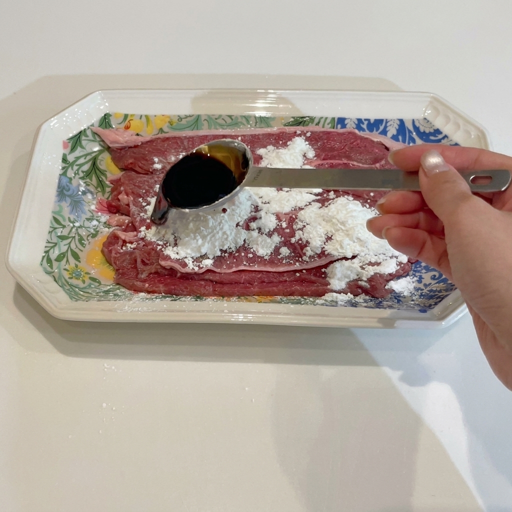 Beef being mixed with soy and oyster sauce in a bowl by hand.