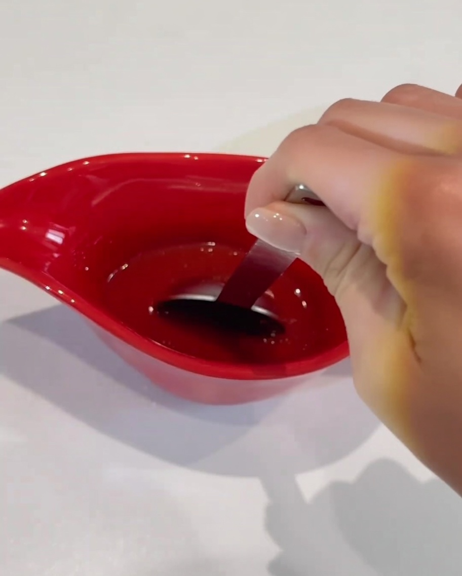 A spoon stirring the prepared red sauce ingredients inside a red gravy boat.