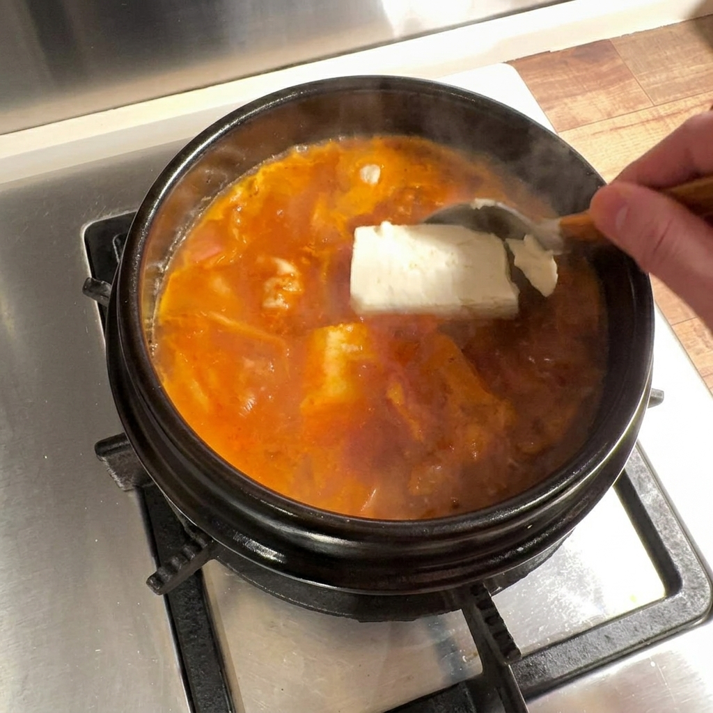 Large pieces of soft tofu being carefully placed into the boiling broth.