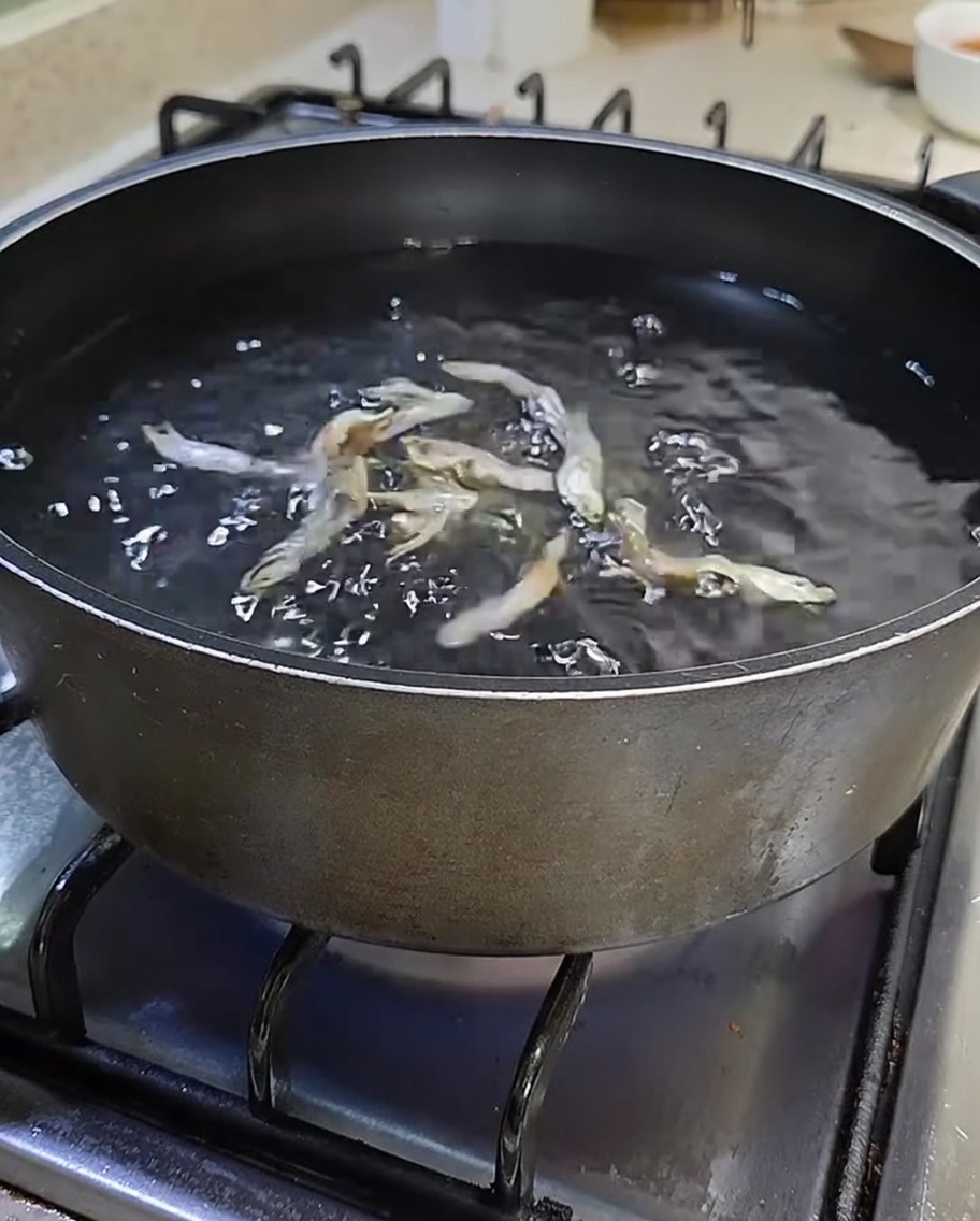 A black pot on a stovetop filled with water and dried silver anchovies.