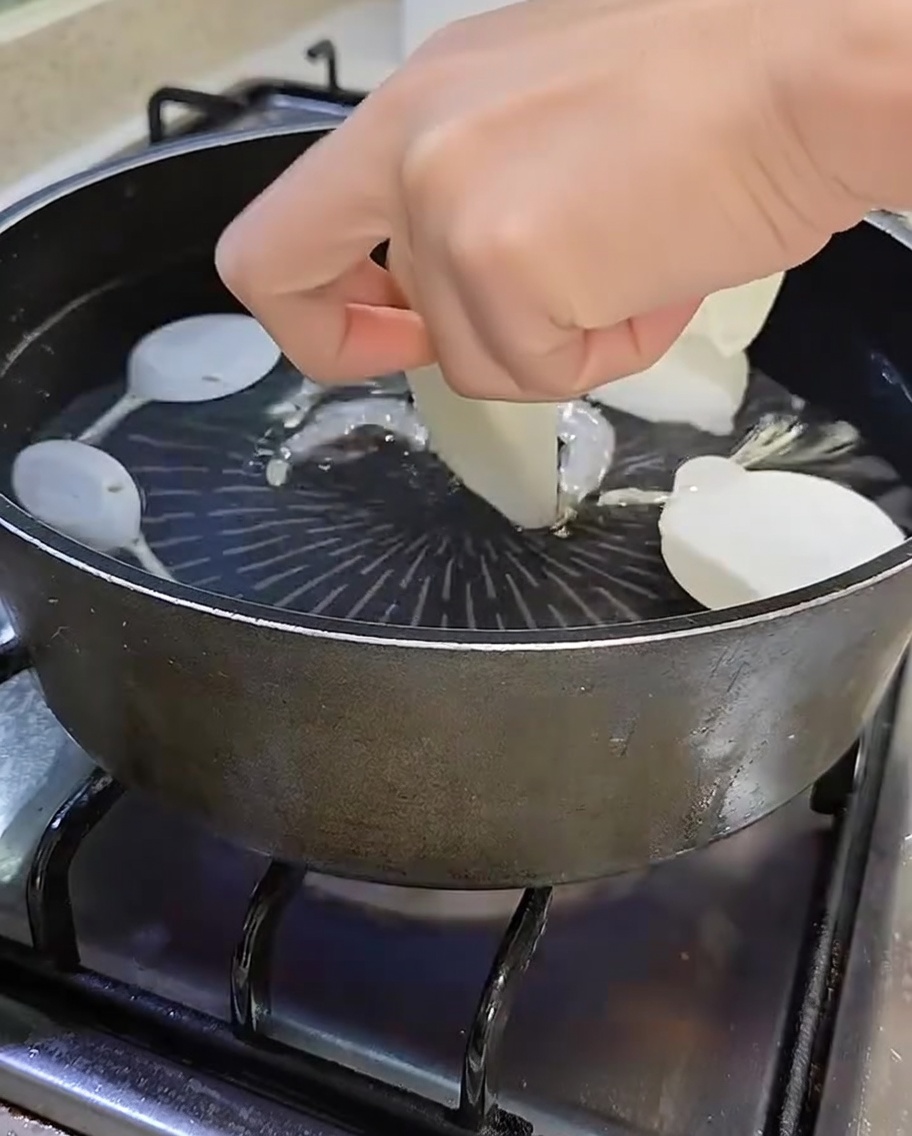 Pot containing boiling water, anchovies, shiitake, sliced radish, and green scallions.