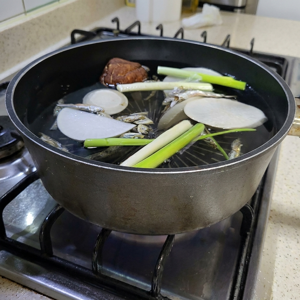 A large piece of dried kelp being added to the boiling pot of broth ingredients.