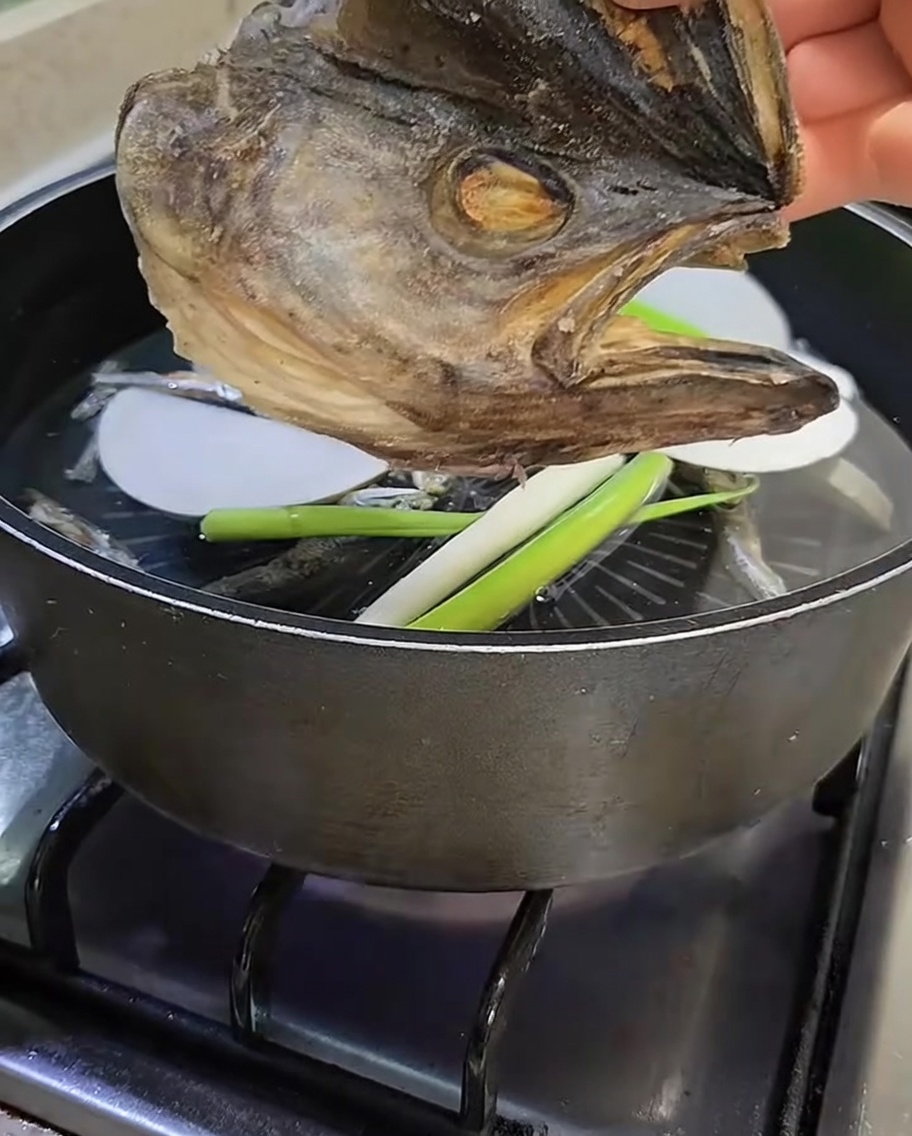 A dried pollack fish head being held over the pot before being added to the broth.