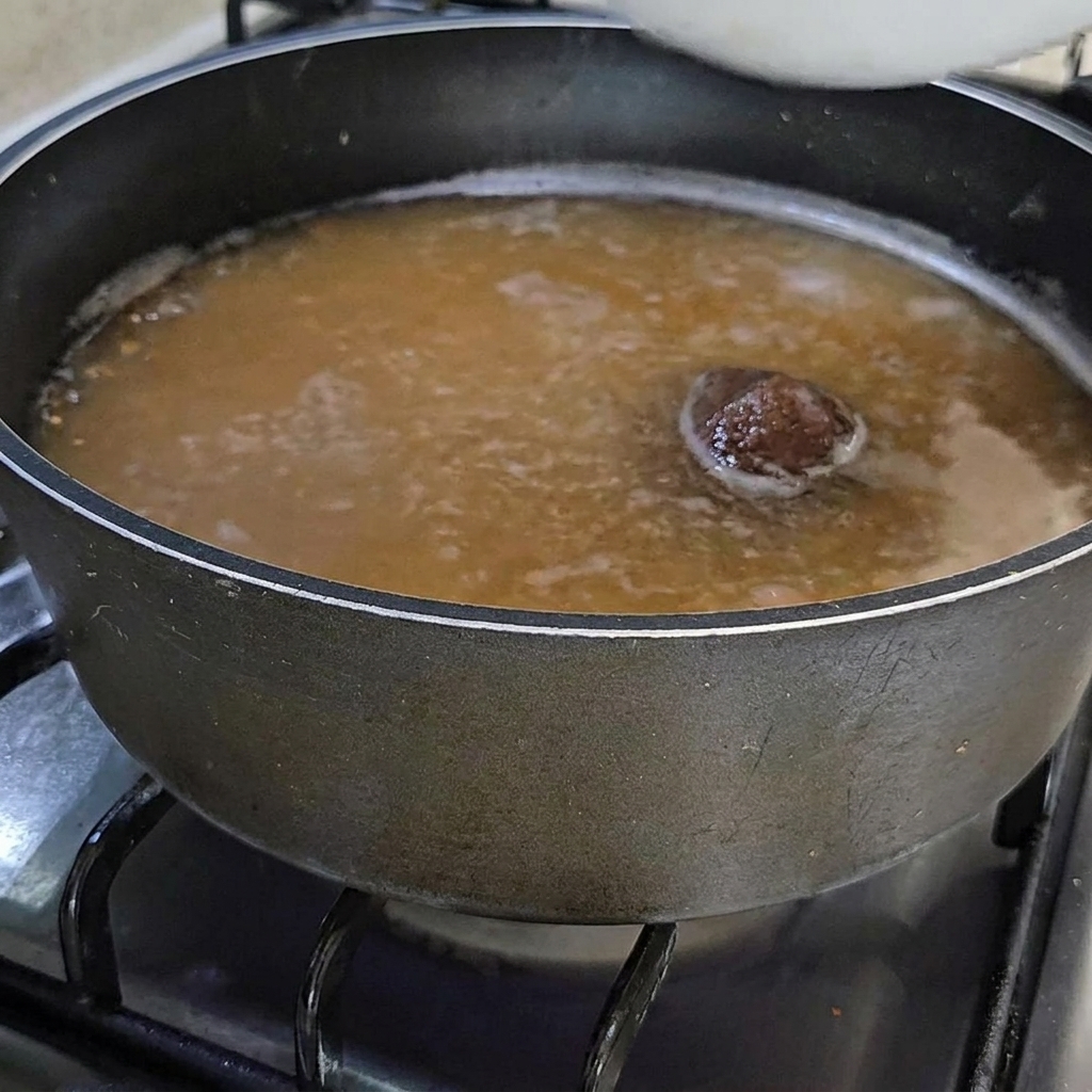A bowl of fresh, orange sea squirts being added to the simmering soybean paste broth.