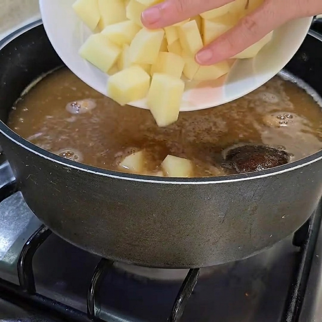 Freshly cubed raw potatoes being added to the pot of simmering broth.