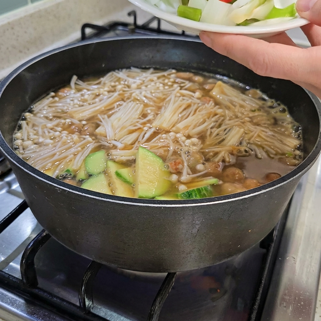 Chopped onions, scallions, and red and green chili peppers being added to the stew, which also contains sliced tofu.
