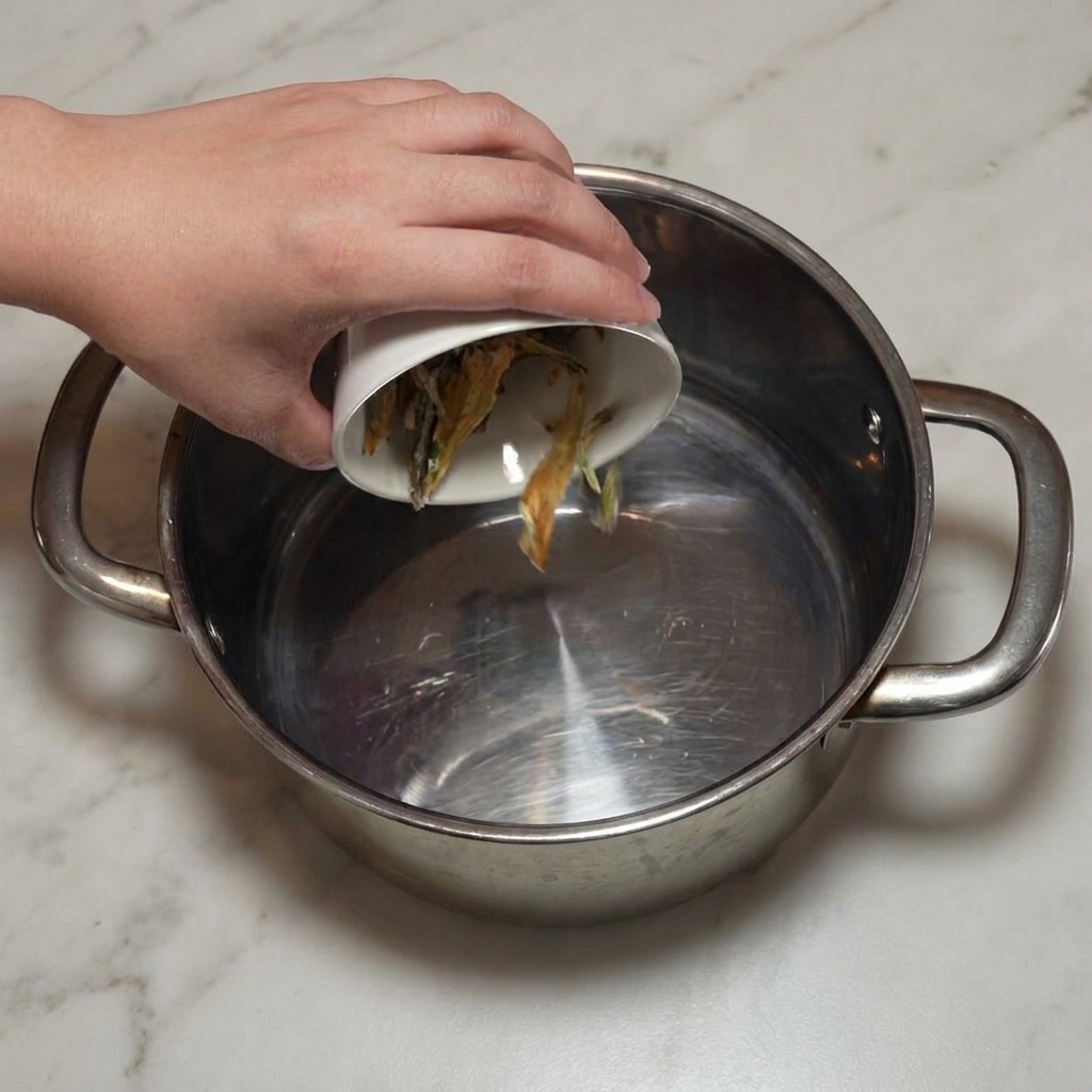 Cleaned dried anchovies being poured into a stainless steel stock pot.