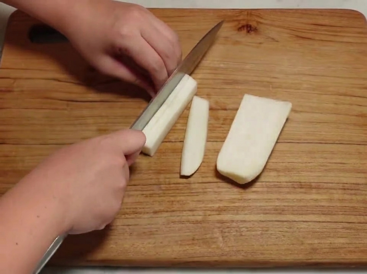 Peeled white radish being chopped into small cubes on a wooden cutting board.