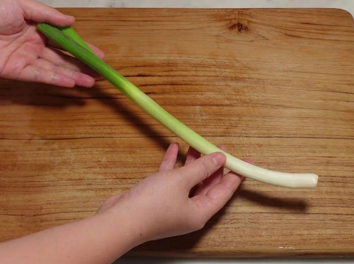 A green onion being sliced into small sections on a wooden cutting board.